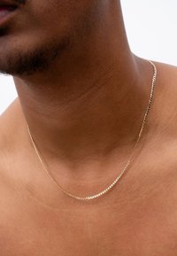 Goldene Kettenhalskette mit gedrehter Design, die auf nackter Haut ruht, mit glatten Gliedern und glänzender Oberfläche.