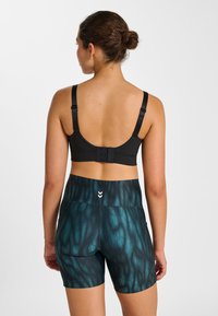 Schwarzer Sport-BH mit verstellbaren Trägern, kombiniert mit türkis gemusterten Shorts mit hohem Bund und kleinem Logodetail auf der Rückseite.