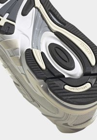 Cipőtalp, amely fehér, szürke és fekete anyagok keverékét tartalmazza; texturált mintázatok; szegmentált gumirészek; és márkajelzések.