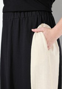 Sort nederdel med elastisk talje, der har en cremefarvet sidelomme lavet af et glat, let stof.