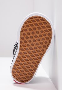 Schwarze Sneaker-Sohle mit einer strukturierten Gummioberfläche, die ein hexagonales Muster aufweist. Weiße Seiten und ein roter Akzent an der Ferse.