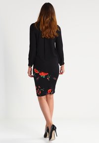 Black long-sleeve top with a floral-patterned, knee-length black skirt. High-heel shoes in black patent leather. Smooth fabric texture.