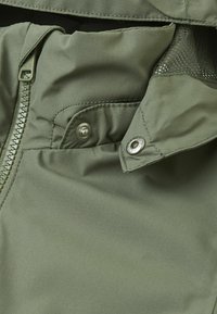 Olive green jacket fabric with a textured finish, featuring a zipper, snap buttons, and a mesh lining in the inner pocket.