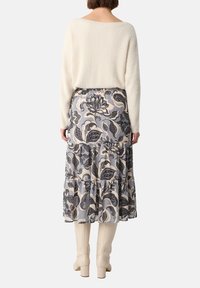 Crème gebreide trui en een gelaagde, enkel-lange rok met een bloemenpatroon in donkerblauw en beige. Korte crème laarzen maken de look compleet.