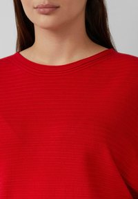 Rode top met verticale ribbeltextuur, ronde halslijn en een ontspannen pasvorm. Gladde stof met een zachte afwerking en subtiele glans.