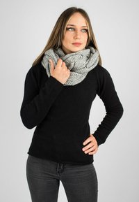 Écharpe infini tricotée en gris clair, en fil texturé. Portée lâchement autour du cou, associée à un haut à manches longues noir et à un jean gris.