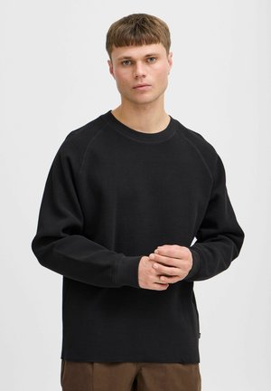 Black long-sleeve shirt with a textured, waffle-knit fabric. Features a crew neck and raglan sleeves. Slightly oversized fit, hem ends at the hips.