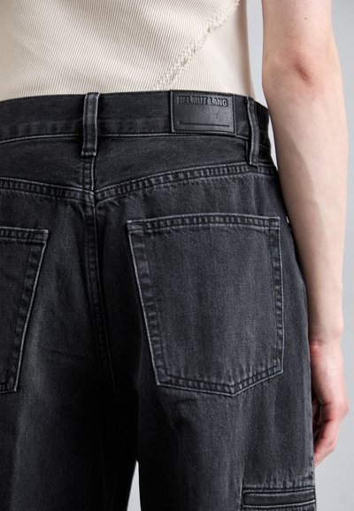 Pantalon en denim noir à coupe droite, avec une étiquette en cuir sur la taille et deux grandes poches arrière. Tissu texturé.