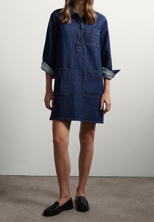Abito camicia in denim blu scuro, con colletto abbottonato, maniche lunghe con polsini arrotolati e due tasche frontali. Tessuto liscio.