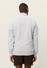 Γκρι φούτερ με ψηλό γιακά, μακριά μανίκια και ριμπ μανσέτες. Απαλή υφή και εφαρμοστή σιλουέτα. Χωρίς εμφανή λογότυπα ή σχέδια.