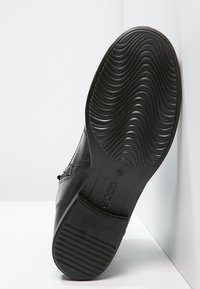 Scarpa in pelle nera con suola in gomma testurizzata caratterizzata da un motivo a onde. Dettagli di cucitura laterale visibili vicino al tallone.