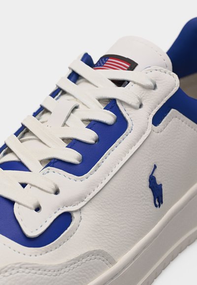 Baskets blanches et bleues avec des lacets blancs, logo brodé d'un joueur de polo bleu sur le côté, et étiquette drapeau américain sur la languette.