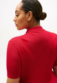 Rotes, geripptes Polohemd mit kurzen Ärmeln, das einen Kragen und eine subtile Textur aufweist, von hinten betrachtet.
