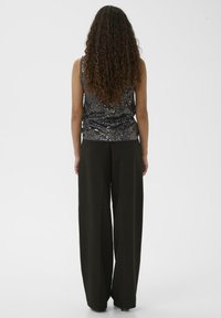 Fekete flitteres trikó, testhezálló szabással, magas derekú, bőszárú fekete nadrággal párosítva. Simogató textúrák és karcsú sziluett.