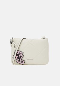 Bílý crossbody batoh vyrobený z hladkého materiálu. Má výraznou černou a růžovou nášivku s logem, zipové uzavření a nastavitelný popruh.