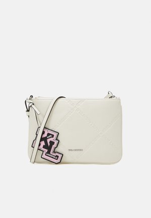 Sac bandoulière blanc en matériau lisse. Présente une grande patch logo noir et rose, une fermeture éclair et une sangle réglable.