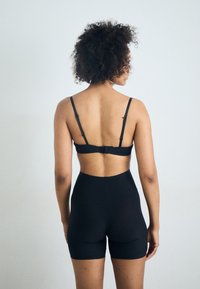 Black sports bra with adjustable straps and hook closure, paired with high-rise black shorts, featuring a smooth, elastic fabric.