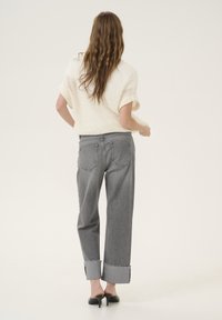Suéter de punto crema de gran tamaño con mangas cortas y corte relajado, combinado con unos vaqueros grises de talle alto con un dobladillo deshilachado. Tacones negros.