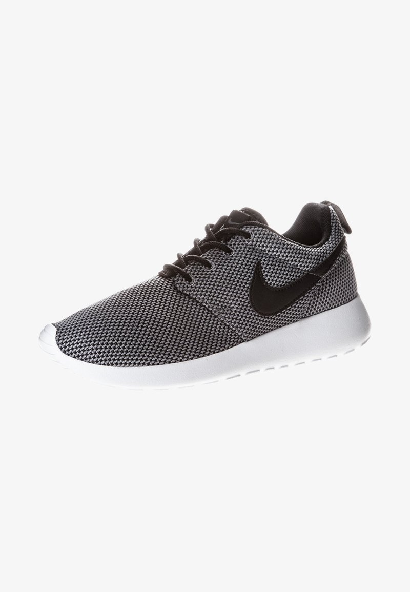 Black and white sneaker with a mesh upper, round toe, and a white rubber sole. Features black Nike logo and lace-up design.