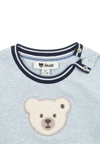 Hellblaues kurzärmeliges Hemd mit einem gestickten Teddybärgesicht in samtiger Textur. Marineblauer, gestreifter, gerippter Ausschnitt und Druckknopfdetails.