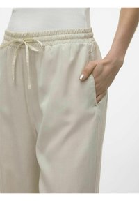 Lahki bež hlače na vrvico z elastičnim pasom, stranskim žepom in gladko teksturo. Rahlo sijajna površina doda prefinjen dodatek.