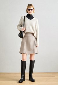 Beżowy sweter dzianinowy z dekoltem w serek, w połączeniu z beżową spódnicą A-line. Czarne skórzane kozaki za kolano oraz mała czarna torba dopełniają stylizację.