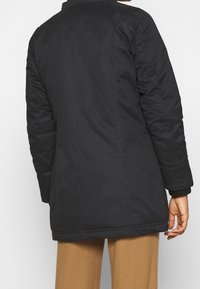 Black insulated coat with a straight cut, long sleeves, and ribbed cuffs. Smooth fabric with minimal visible seams, no embellishments.