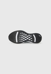 Schwarze Sportschuhsohle mit strukturiertem Muster, versehen mit weißen Akzenten und einem Logo, vor einem schlichten weißen Hintergrund platziert.