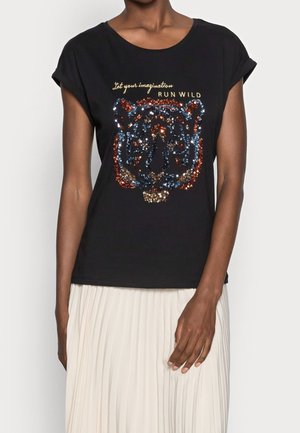 Vrouw draagt een zwart T-shirt met een kleurrijk pailletten tijgergezicht en de tekst "Laat je verbeelding de vrije loop," gecombineerd met een witte geplooide rok.