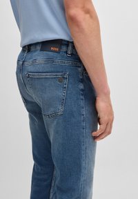 Tmavě modré džíny z denimu s přímým střihem, s nášivkou loga na pase a jemným vyběláním na zadních kapsách.