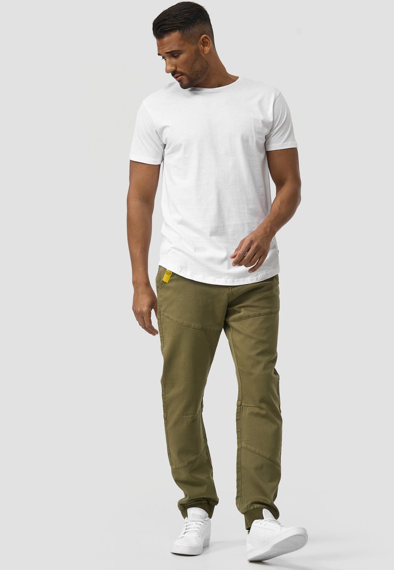 T-shirt blanc à manches courtes et pantalon cargo vert olive avec de multiples poches. Baskets blanches, coupe décontractée, design jambes droites, accents cousus.