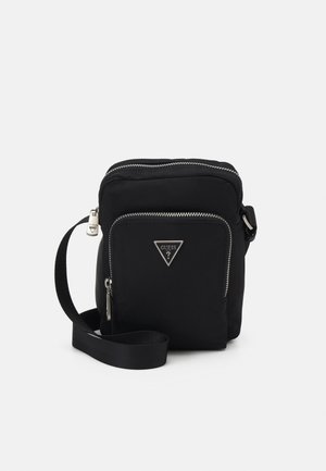 Black small crossbody bag with front zip pocket, silver zippers, adjustable strap, and triangular Guess logo on front pocket.