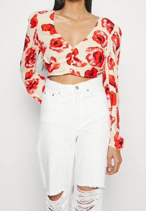 Bloemige cropped blouse in crème met rode klaprozenprint, met een v-hals en knoopsluiting. Gecombineerd met hoge taille witte ripped jeans.