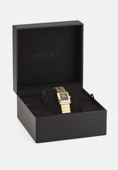 Gold-tone Versace watch with a square black face, metallic band, and textured links, displayed in a black velvet-lined box.