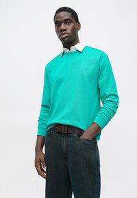 Türkiissinine pikkade varrukatega särk valge kraega, kombineeritud tumedate teksade ja pruuni vööga. Lihtne disain, sile tekstuur ja vormis lõige.