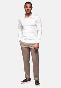 Witte langemouwen polo met horizontale lichtbruine strepen, gecombineerd met lichtbruine broek en donkerbruine schoenen. Eenvoudig en slim passend ontwerp.