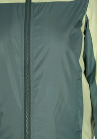 Groene en lichtgroene ritsjack met een gladde textuur, voorzien van een centrale rits, zijzakken en contrasterende panelen.