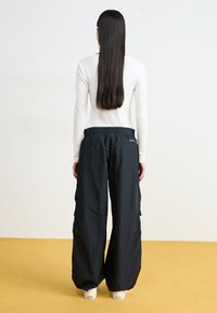 Svarte cargo bukser laget av lett materiale, med bred ben design og elastisk midje, med sidelommer for praktisk bruk.