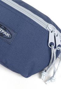 Astuccio per matite di colore blu con superficie testurizzata, dotato di chiusura con doppia cerniera e lacci grigi. Il logo del marchio è visibile sul lato.