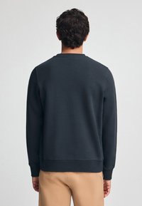 Sudadera de un azul marino oscuro con una textura suave, escote redondo y puños y dobladillo de canalé, combinada con pantalones beige.