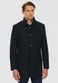 Granatowy wełniany płaszcz o prostym kroju, z stójką, dwiema przednimi kieszeniami i zapięciem na guziki. Posiada subtelne przeszycia na ramionach oraz fakturowany materiał.