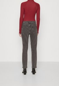 Jeans de mezclilla gris con un corte ajustado, combinados con una blusa de manga larga burdeos. Botines negros de tacón acentúan el atuendo. Se muestra la vista posterior.