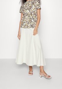 Top corto de manga corta con estampado floral en color crema, combinado con una falda midi blanca y fluida. El conjunto se completa con unos tacones blancos con tiras.