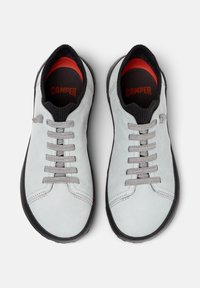 Light grey suede sneakers with grey laces, black rubber soles, and a red accent inside the collar. Features a rounded toe design.