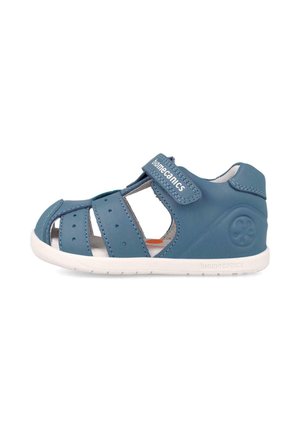 Sandalia de cuero azul para niños pequeños con punta cerrada, tiras recortadas, correa de Velcro etiquetada "biomecanics" y suela blanca flexible.