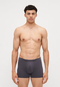 Szürke pamut boxeralsó, testhez simuló kivitelben, rugalmas derekú, látható minták nélkül. Egy férfi modell viseli fehér háttér előtt.
