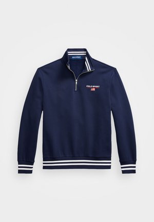 Granatowy sweter z zamkiem ozdobionym wysokim kołnierzem, białymi paskami na mankietach i dole oraz haftowanym logo "POLO SPORT" na klatce piersiowej.