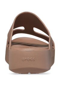 Braune Crocs-Sandalen mit breitem Riemen und strukturiertem Finish. Die Unterseite zeigt den Markennamen und die Sohle hat ein erhabenes Muster.