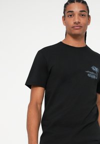 Čierne bavlnené tričko s krátkymi rukávmi, okrúhlym výstrihom a modrým dizajnom palmy na ľavej strane hrudníka s textom "RIPCURL".
