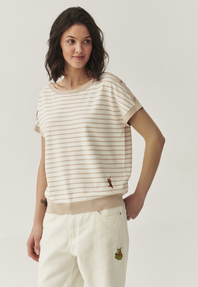 Haut beige rayé à manches courtes, avec un ourlet côtelé et des détails en boutons. Présente des accents brodés près du bas. Associé à un pantalon blanc.